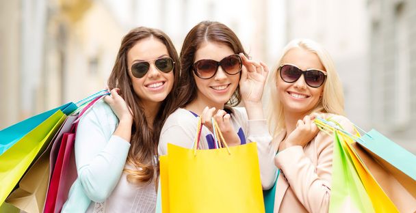 three smiling girls with shopping bags in ctiy - Foto, imagen