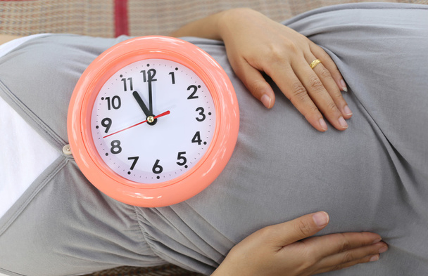 Těhotné ženy ukazují hodiny na břiše sdělit čas. - Fotografie, Obrázek
