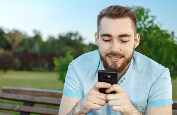 Smiling young man texting on the cellphone - Fotó, kép