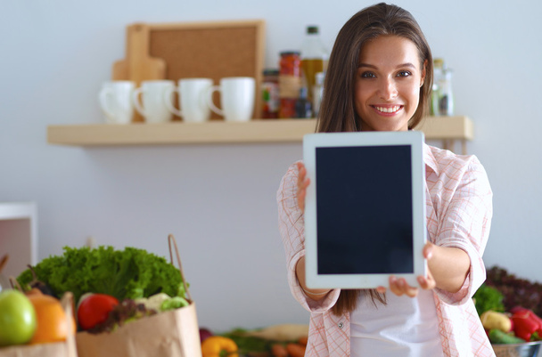 Young woman using a tablet computer to cook in her kitchen - Foto, Imagen