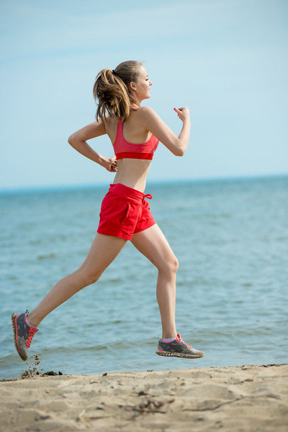 Young lady running at the sunny summer sand beach. Workout.  Jog - Foto, imagen