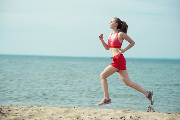 Young lady running at the sunny summer sand beach. Workout.  Jog - Foto, Bild