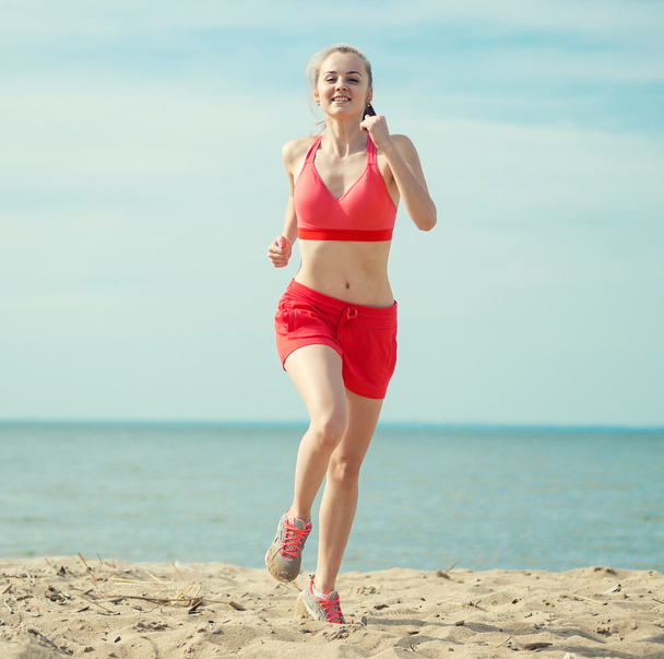 Young lady running at the sunny summer sand beach. Workout.  Jog - Fotó, kép