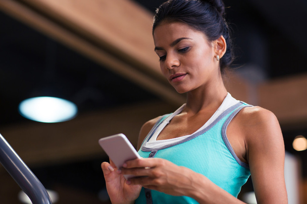 Woman using smartphone in fitness gym - Foto, afbeelding