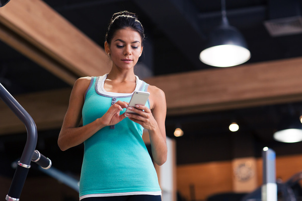 Woman using smartphone in fitness gym - Photo, Image