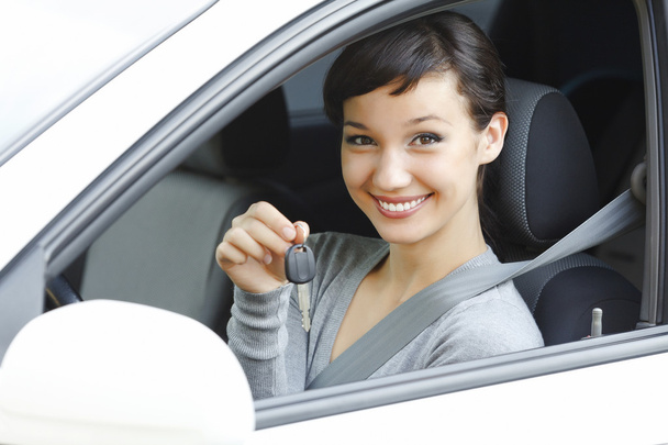 Nätti naiskuljettaja valkoisessa autossa näyttää auton avaimen
 - Valokuva, kuva