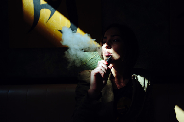 Девушка сидит и курит электронную сигарету
 - Фото, изображение