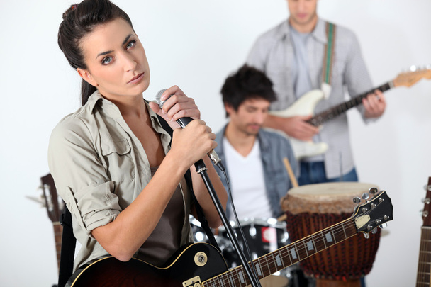 Brunette singer with guitar and microphone and male musicians in background - Foto, Imagem