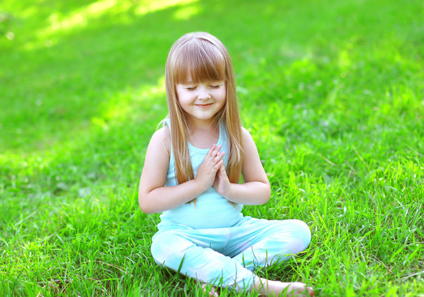 Child doing yoga exercises sitting on the grass in sunny summer  - Fotó, kép