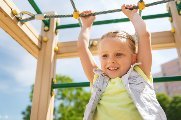 fröhliches kleines Mädchen klettert auf Kinderspielplatz - Foto, Bild