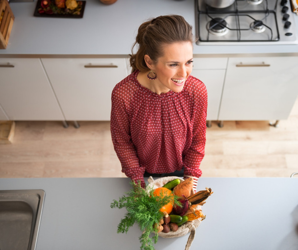 From above, smiling woman in kitchen with fall vegetables - Фото, изображение