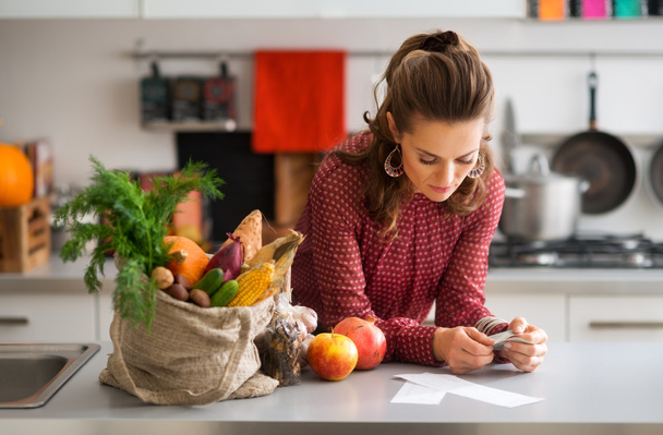 Woman in kitchen reading shopping list with shopping and receipt - Foto, Bild