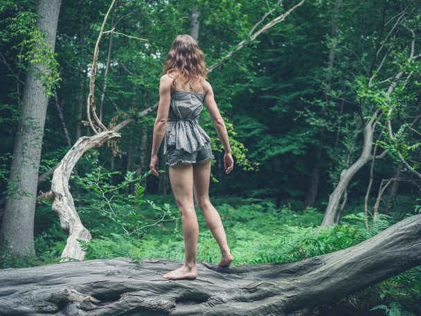 Barefoot woman standing on a fallen tree in the forest - Фото, зображення