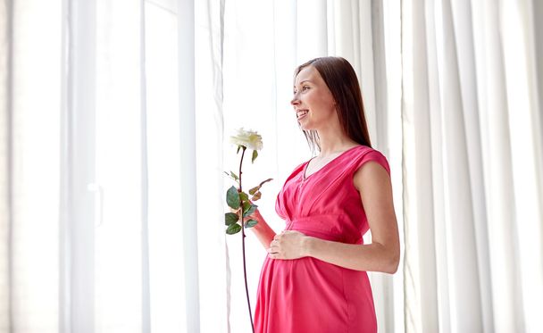 happy pregnant woman with rose flower at home - Foto, imagen