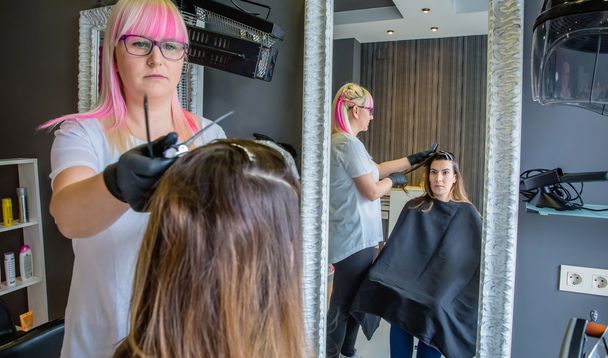 Woman looking in mirror to hairdresser combing hair - Photo, Image