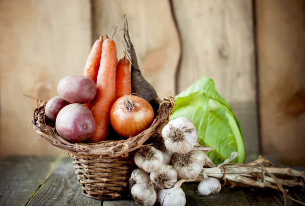 Raw vegetables in a basket on a wooden table. - Фото, зображення