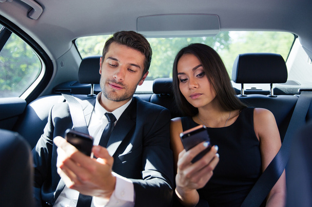 Businessman and businesswoman using smartphone in car - 写真・画像