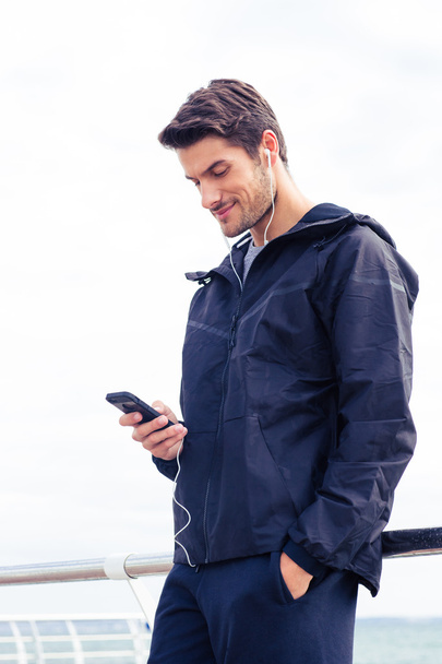 Man using smartphone with headphones outdoors  - Фото, изображение