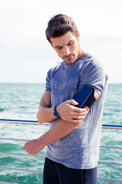 Male runner listening to music adjusting settings on armband for smartphone - Foto, immagini