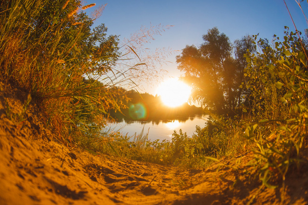Zand gras weg daalt naar de rivier meer bij zonsondergang de zon se - Foto, afbeelding