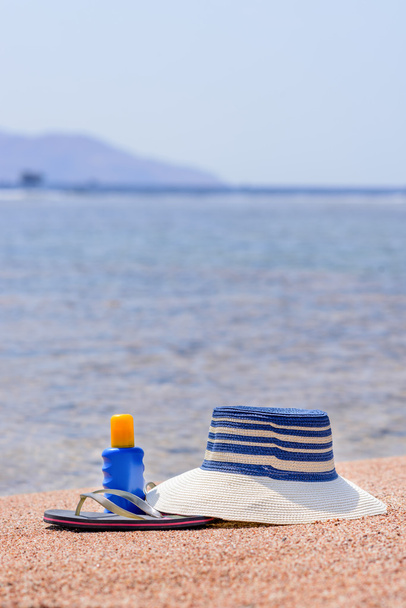 Sombrero de sol, tangas y protector solar en una playa
 - Foto, Imagen