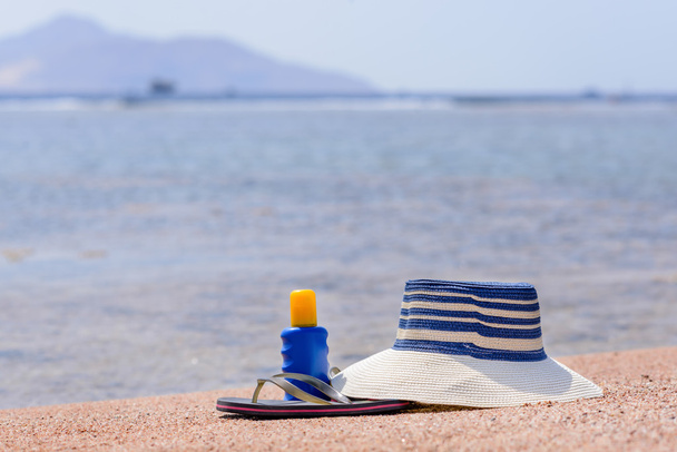 Chapéu de sol, tangas e protetor solar em uma praia
 - Foto, Imagem