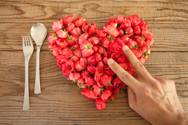 Heart made of red roses in wooden background, covered by an hand - Photo, Image