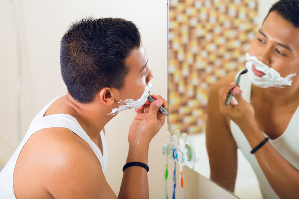 Азиатский мужчина бреется перед зеркалом
 - Фото, изображение