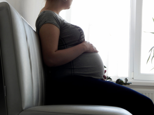 Mujer embarazada sentada en el sofá en el hospital y esperando cita ginecológica
 - Foto, Imagen