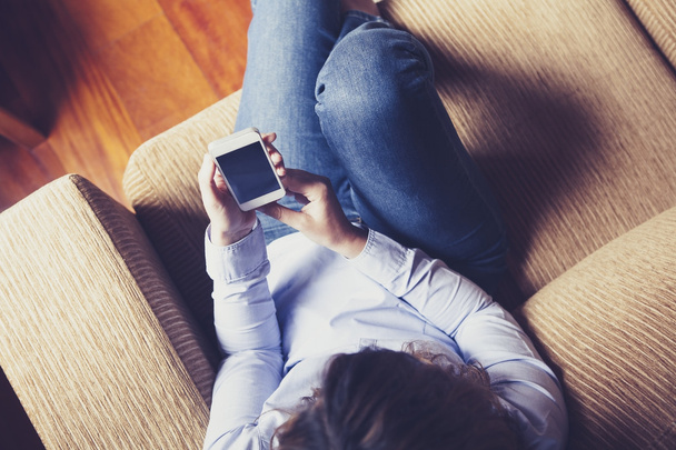 Aerial view of girl reading a phone while sitting in a couch. - Foto, Imagen