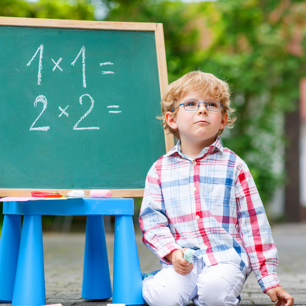Cute little kid boy with glasses at blackboard practicing mathem - Fotó, kép
