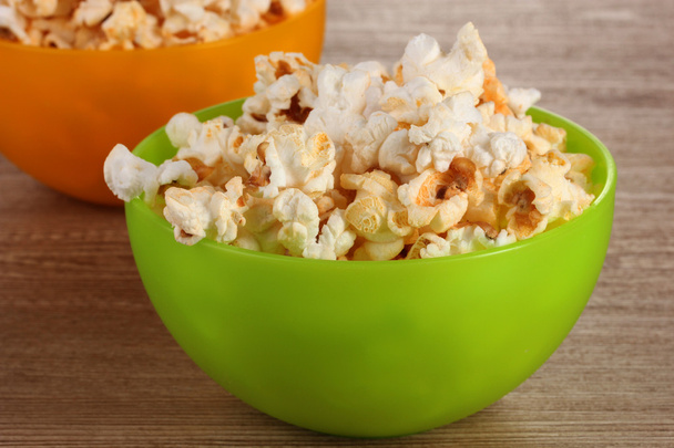 Popcorn in bright plastic bowls on wooden table - Photo, image