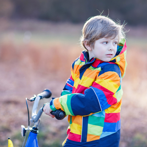 kid boy in safety helmet and colorful raincoat riding bike, outd - Photo, Image