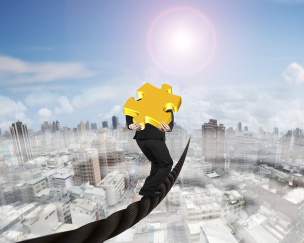 Businessman carrying 3D gold puzzle piece balancing on wire - Foto, afbeelding