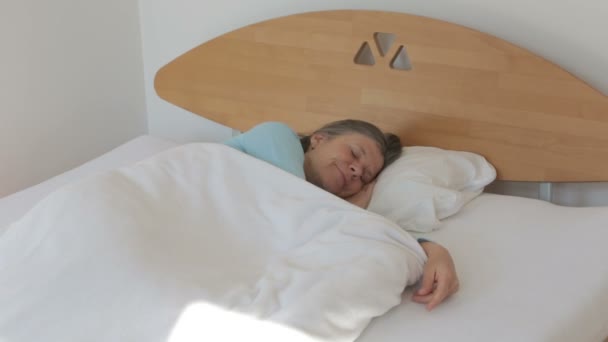 woman in her 50s waking up with a headache - Materiał filmowy, wideo
