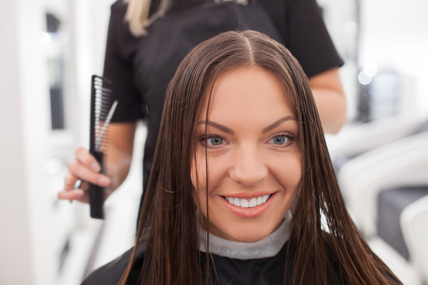 Cheerful young hairdresser is cutting hair of her client - Foto, Bild
