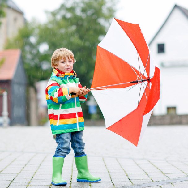 Little blond kid boy walking with big umbrella outdoors  - Photo, Image