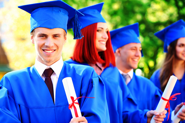 Graduierte Studenten in Diplomhüten und -kleidern, im Freien - Foto, Bild