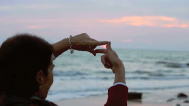 femme encadre le soleil avec ses mains au coucher du soleil sur la plage
 - Séquence, vidéo