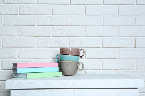 Books with cups on brick wall background - 写真・画像