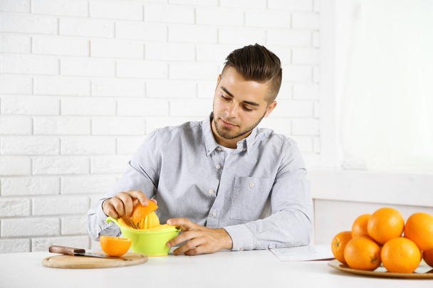 Young man using citrus-fruit squeezer, preparing orange juice - Zdjęcie, obraz