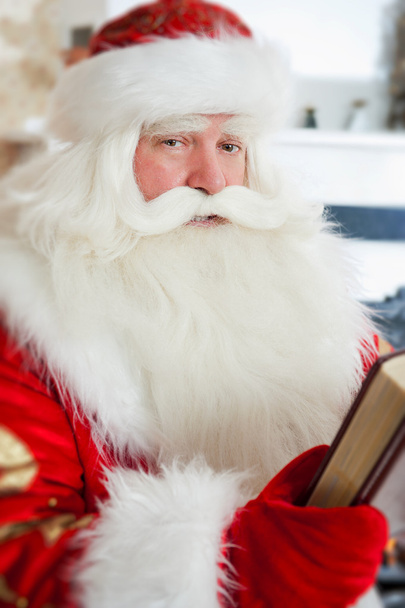Santa sitting at the Christmas tree, near fireplace and reading - Zdjęcie, obraz