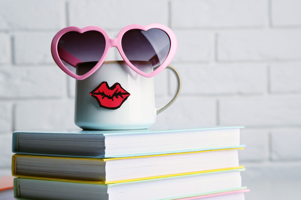 Books and cup with lips on wooden table on brick wall background - Foto, Imagem