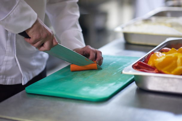 chef in hotel kitchen slicing vegetables with knife - Foto, afbeelding