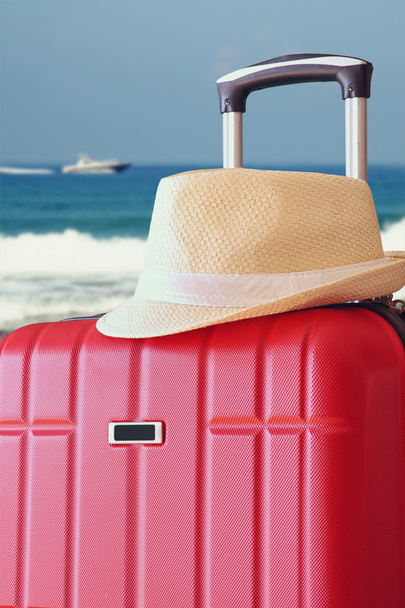 image of red elegant travel luggage and fedora hat  in front of sea. travel and vacation concept - Fotó, kép