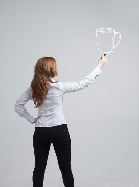 young woman draws a Cup of coffee on grey background - Foto, afbeelding