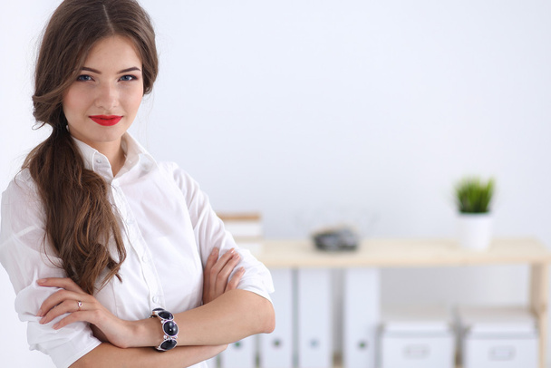 Attractive businesswoman standing near wall in office - Foto, afbeelding