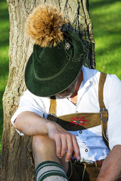 bavarian man sitting by a tree and sleeps - Foto, afbeelding