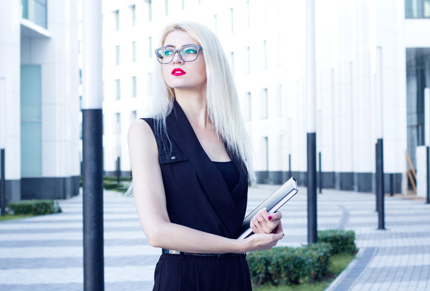 Intelligent blond with red lips and notebook looks into the distance on the background of the business center - 写真・画像