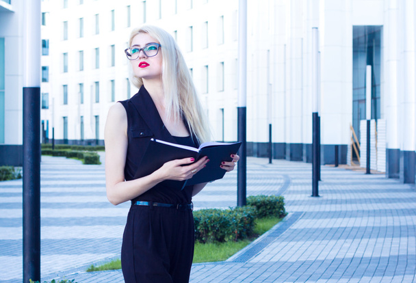 Business woman with a notebook looking into the distance on the background of the business center - 写真・画像
